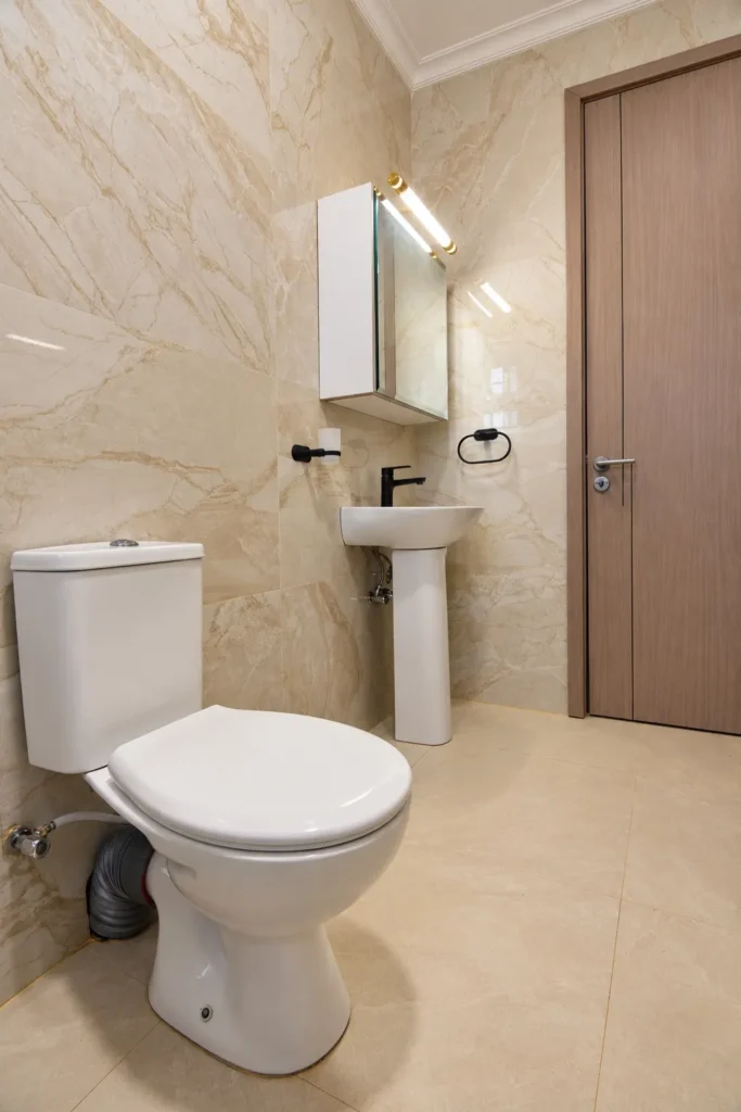 Close-coupled toilet and pedestal basin with black tap and marble-effect wall tiles, Kilimambogo